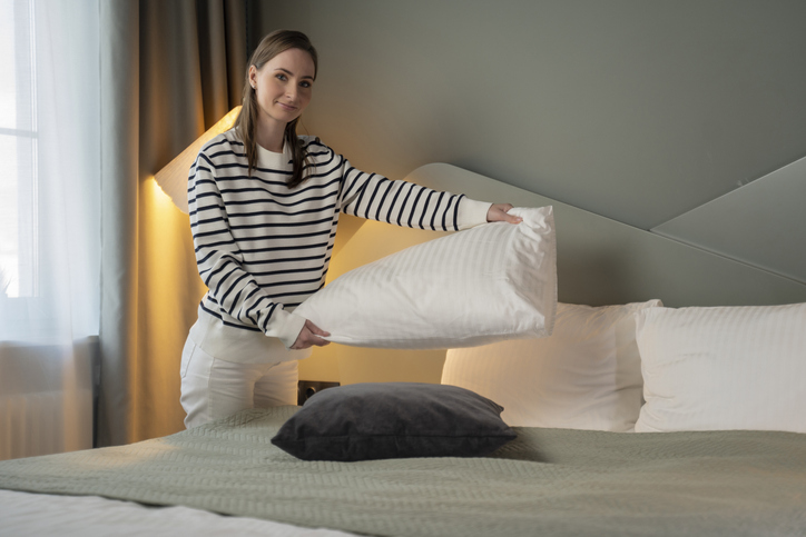 Woman doing her morning routine, arranging pillows and making up bed at home